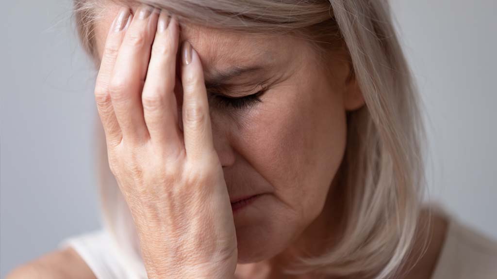 woman with hand to forehead eyes closed experiencing stress